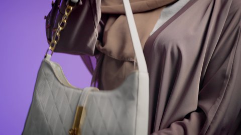 Close-up of a veiled young Saudi Arabian Gulf woman holding a bag with happy gestures, displaying luxury international bag models, women's fashion and accessories, an Emirati woman wearing a modern Gulf abaya, the concept of fashion and elegance.