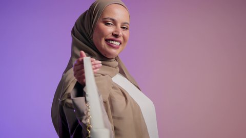 Display of luxury international handbag models, women's fashion and accessories. A close-up of a veiled young Saudi Arabian Gulf woman holding a bag with happy gestures. An Emirati woman wearing a modern Gulf abaya. The concept of fashion and elegance.