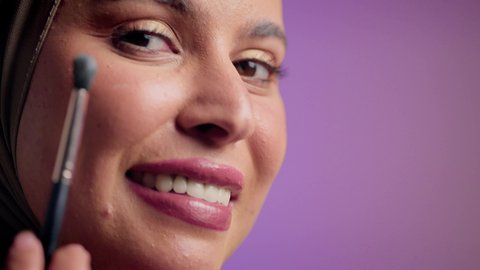 Marketing for beauty products, a photograph of a Saudi Arabian Gulf woman wearing an abaya and hijab holding a blush brush, an Emirati woman using modern women's cosmetics, the concept of femininity and attention to one's outward appearance, makeup tutorial, a high-end women's salon, a colorful background.