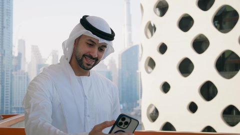 Taking selfies with a mobile phone, documenting happy moments, using a modern and advanced technical device to immortalize memories, a close-up of a smiling Emirati Gulf Arab man wearing a white kandura and ghutra holding a mobile phone and taking a commemorative selfie with gestures of pleasure
