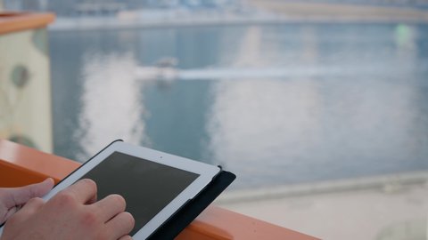 Working remotely via the Internet, a modern and advanced technical device, communicating with family and friends via a tablet, a close-up of the hands of an Arab Gulf Emirati man using a portable tablet, a background of towers and skyscrapers in the Emirates