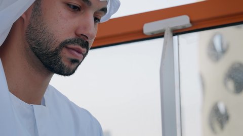 تناول الأعشاب الدافئة، الاستمتاع بالمشروبات الساخنة، تصوير مقرب لرجل عربي خليجي اماراتي يرتدي الكندورة والغترة البيضاء يقوم بشرب القهوة في المقهى، قضاء وقت الفراغ باحتساء المشروب المفضل