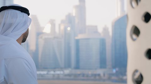 الاستمتاع بالمشروبات الساخنة، تصوير مقرب لرجل عربي خليجي اماراتي يرتدي الكندورة والغترة البيضاء يقوم بشرب القهوة في المقهى، قضاء وقت الفراغ باحتساء المشروب المفضل، تناول الأعشاب الدافئة، الأبراج وناطحات السحاب في الامارات