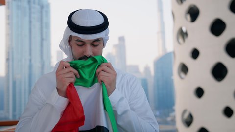 يوم العلم 3 نوفمبر، حب الوطن والاعتزاز به، اليوم الوطني الاماراتي 1971، الاحتفال بذكرى تأسيس الاتحاد 2 ديسمبر في الخارج، تصوير مقرب لرجل عربي خليجي اماراتي يرتدي الكندورة والغترة يقوم بتقبيل علم الامارات العربية المتحدة