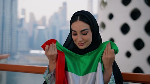 UAE National Day 1971, Flag Day November 3, love and pride of the homeland, celebration of the founding anniversary of the Union December 2 abroad, close-up of a veiled Emirati Gulf Arab woman wearing an abaya kissing the flag of the United Arab Emirates