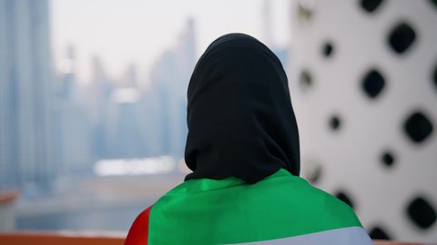 Celebrating the anniversary of the founding of the Union, December 2, abroad, UAE National Day 1971, Flag Day, November 3, love and pride of the homeland, close-up from the back of a veiled Emirati Gulf Arab woman wearing an abaya, placing the flag of the United Arab Emirates on her shoulders