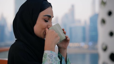 الاستمتاع بالمشروبات الساخنة، ايماءات المتعة والاسترخاء، قضاء وقت الفراغ باحتساء المشروب المفضل, تناول الأعشاب الشتوية الدافئة، تصوير مقرب لامراة اماراتية ترتدي العباءة والحجاب تقوم بشرب القهوة