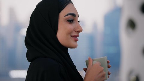 الاستمتاع بالمشروبات الساخنة، ايماءات المتعة والتلذذ باحتساء المشروب المفضل, تناول الأعشاب الشتوية الدافئة، تصوير مقرب لامراة اماراتية ترتدي العباءة والحجاب تقوم بشرب القهوة، قضاء وقت ممتع في الخارج