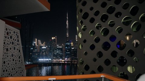 الأناقة والاهتمام بالمظهر الخارجي، قضاء وقت ممتع في الخارج, تصوير مقرب من الخلف لرجل عربي خليجي إماراتي يرتدي الغترة والكندورة الاماراتية البيضاء يقوم بتأمل الأبراج وناطحات السحاب المضاءة في وقت الليل في الامارات