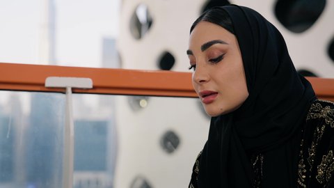 اجراء مكالمة هاتفية عبر جهاز الجوال، التواصل وتبادل الأحاديث والأخبار مع الأهل والأصدقاء،  تصوير مقرب لامراة اماراتية ترتدي العباءة والحجاب تمسك بيدها الهاتف المحمول وتشرب القهوة، استخدام جهاز تقني حديث ومتطور، احتساء المشروب المفضل في المقهى