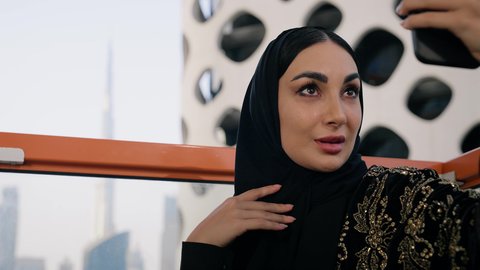 توثيق اللحظات التذكارية السعيدة، استخدام جهاز تقني حديث ومتطور لتخليد الذكريات ، التقاط الصور الشخصية باستخدام الهاتف المحمول، تصوير مقرب لامراة اماراتية ترتدي العباءة والحجاب تأخذ صورة سيلفي بإيماءات السعادة والسرور