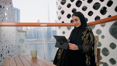 احتساء المشروب المفضل في الكافيه، ادارة الأعمال وانجاز المهام المطلوبة، العمل عن بعد، مهنة ووظيفة نسائية، تصوير مقرب لإمرأة عربية خليجية اماراتية محجبة ترتدي عباءة ملونة تستخدم الجهاز اللوحي وتشرب القهوة، استخدام جهاز تقني حديث ومتطور