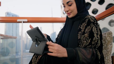 تعابير التركيز والاندماج، ادارة الأعمال وانجاز المهام المطلوبة، العمل عن بعد،  مهنة ووظيفة نسائية،  تصوير مقرب لإمرأة عربية خليجية اماراتية محجبة ترتدي عباءة سوداء تستخدم الحاسوب المحمول، استخدام جهاز تقني حديث ومتطور