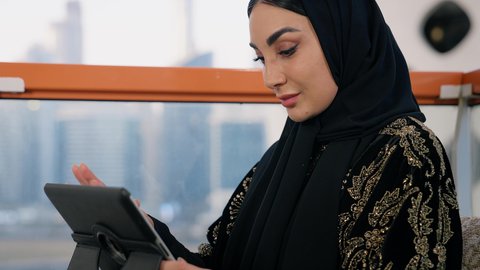 Gestures of focus and integration, business management and completing required tasks, remote work, female profession and job, close-up of a veiled Emirati Gulf Arab woman wearing a black abaya using a laptop, using a dern and advanced technical device