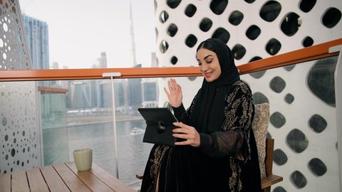 ادارة الأعمال وانجاز المهام المطلوبة، العمل عن بعد، مهنة ووظيفة نسائية، تصوير مقرب لإمرأة عربية خليجية اماراتية محجبة ترتدي عباءة ملونة تستخدم الجهاز اللوحي وتشرب القهوة، استخدام جهاز تقني حديث ومتطور، احتساء المشروب المفضل في الكافيه