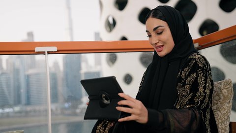 العمل عن بعد،  مهنة ووظيفة نسائية،  تصوير مقرب لإمرأة عربية خليجية اماراتية محجبة ترتدي عباءة سوداء تستخدم الحاسوب المحمول، استخدام جهاز تقني حديث ومتطور، ايماءات التركيز والاندماج، ادارة الأعمال وانجاز المهام المطلوبة