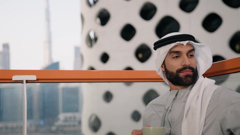 توثيق اللحظات السعيدة، التقاط الصور الشخصية باستخدام الجوال، استخدام جهاز تقني حديث ومتطور في تخليد الذكريات، تصوير مقرب لرجل عربي خليجي اماراتي يرتدي الكندورة والغترة البيضاء يمسك الهاتف المحمول ويأخذ صورة سيلفي بإيماءات السرور