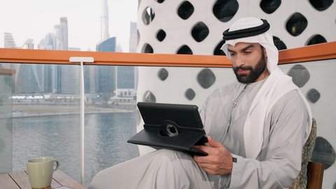 تعابير السرور والسعادة، استخدام جهاز تقني حديث ومتطور، تصوير مقرب لرجل عربي خليجي اماراتي يرتدي الكندورة والغترة البيضاء يستخدم الجهاز اللوحي، إنجاز مهام العمل عن بعد، إدارة شؤون الأعمال وتنظيمها عبر الايباد