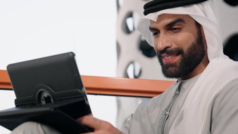 Expressions of joy and happiness, using a modern and advanced technical device, a close-up of an Emirati Gulf Arab man wearing a white kandura and ghutra using a tablet, completing work tasks remotely, managing and organizing business affairs via an iPad
