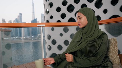 كافيهات ومطاعم في الامارات العربية المتحدة، قضاء وقت الفراغ باحتساء المشروب المفضل, تناول الأعشاب الشتوية الدافئة، الاستمتاع بالمشروبات الساخنة، تصوير مقرب لامراة اماراتية ترتدي العباءة والحجاب تجلس على اريكة مريحة تقوم بشرب القهوة في المقهى