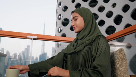 كافيهات ومطاعم في الامارات العربية المتحدة، قضاء وقت الفراغ باحتساء المشروب المفضل, تناول الأعشاب الشتوية الدافئة، الاستمتاع بالمشروبات الساخنة، تصوير مقرب لامراة اماراتية ترتدي العباءة والحجاب تجلس على اريكة مريحة تقوم بشرب القهوة في المقهى