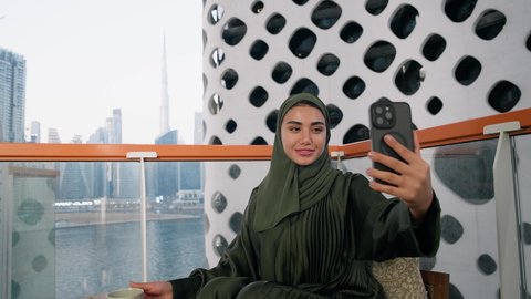 Taking selfies with a mobile phone, a close-up of an Emirati woman wearing an abaya and hijab taking a selfie with happy and joyful gestures, documenting happy memorial moments, using a modern and advanced technical device to immortalize memories