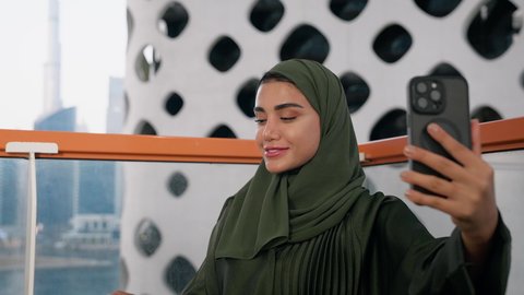 Documenting happy memorable moments, using a modern and advanced technical device to immortalize memories, taking personal photos using a mobile phone, a close-up of an Emirati woman wearing an abaya and hijab taking a selfie with gestures of happiness and pleasure
