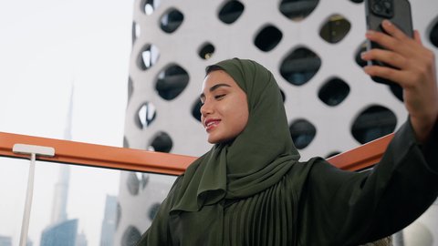 توثيق اللحظات التذكارية السعيدة، استخدام جهاز تقني حديث ومتطور لتخليد الذكريات ، التقاط الصور الشخصية باستخدام الهاتف المحمول، تصوير مقرب لامراة اماراتية ترتدي العباءة والحجاب تأخذ صورة سيلفي بإيماءات السعادة والسرور