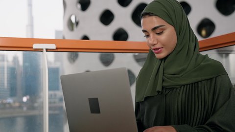 Women's job and profession, close-up of a veiled Emirati Gulf Arab woman wearing a colorful abaya using a laptop, using a modern and advanced technical device, gestures of concentration and integration, business management and completing required tasks, working remotely