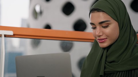 مهنة ووظيفة نسائية،  تصوير مقرب لإمرأة عربية خليجية اماراتية محجبة ترتدي عباءة ملونة تستخدم الحاسوب المحمول، استخدام جهاز تقني حديث ومتطور، ايماءات التركيز والاندماج، ادارة الأعمال وانجاز المهام المطلوبة، العمل عن بعد