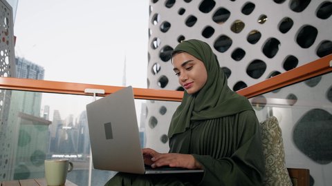 Women's job and profession, close-up of a veiled Emirati Gulf Arab woman wearing a colorful abaya using a laptop, using a modern and advanced technical device, gestures of concentration and integration, business management and completing required tasks, working remotely