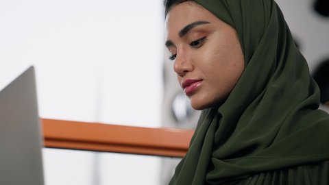 مهنة ووظيفة نسائية،  تصوير مقرب لإمرأة عربية خليجية اماراتية محجبة ترتدي عباءة ملونة تستخدم الحاسوب المحمول، استخدام جهاز تقني حديث ومتطور، ايماءات التركيز والاندماج، ادارة الأعمال وانجاز المهام المطلوبة، العمل عن بعد