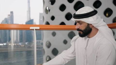 تناول الأعشاب الشتوية الدافئة، الاستمتاع بالمشروبات الساخنة، تصوير مقرب لرجل عربي خليجي اماراتي يرتدي الكندورة والغترة البيضاء يجلس على اريكة مريحة يقوم بشرب القهوة في المقهى، إيماءات السعادة والسرور، قضاء وقت الفراغ باحتساء المشروب المفضل