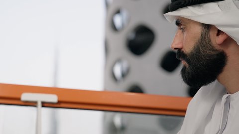 قضاء وقت الفراغ باحتساء المشروب المفضل, تناول الأعشاب الشتوية الدافئة، الاستمتاع بالمشروبات الساخنة، تصوير مقرب لرجل عربي خليجي اماراتي يرتدي الكندورة والغترة البيضاء يجلس على اريكة مريحة يقوم بشرب القهوة في المقهى، إيماءات السعادة والسرور