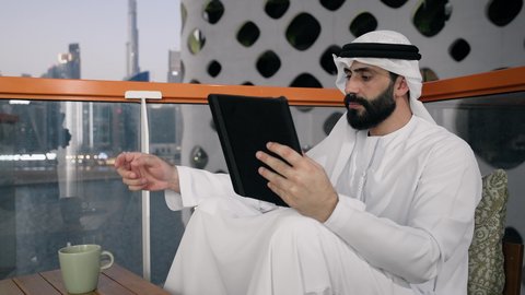 Accomplishing work tasks remotely, managing and organizing business affairs via iPad, gestures of pleasure and happiness, using a modern and advanced technical device, a close-up of an Emirati Gulf Arab man wearing a white kandura and ghutra using a tablet