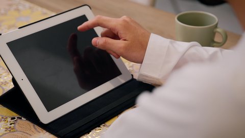 مشاهدة الافلام والمسلسلات ، تصفح التطبيقات والمواقع، الاستمتاع بالمشروبات الساخنه ، عقد إجتماع عمل عبر الإنترنت، تصوير مقرب لرجل عربي خليجي اماراتي يرتدي الكندورة والغتره يجلس في المنزل، جلسة عمل عن بعد، جلسات هادئة في المنزل، استخدام جهاز التابلت