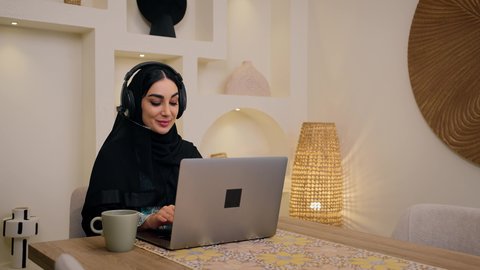 مشاهدة الافلام والمسلسلات ، تصفح التطبيقات والمواقع، الاستمتاع بالمشروبات الساخنه ، عقد إجتماع عمل عبر الإنترنت، الاستماع الى الموسيقي عبر سماعات الاذن ،تصوير مقرب لامرأة عربية خليجية سعودية ترتدي العباءه والحجاب تجلس في المنزل، جلسة عمل عن بعد، جلسات هادئة في المنزل، سيدة اماراتيه تستخدم جهاز الحاسوب المحمول