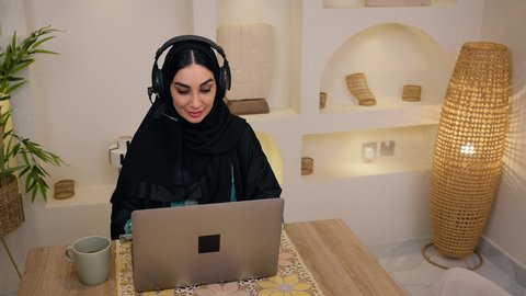 جلسة عمل عن بعد، الاستمتاع بالمشروبات الساخنه ، عقد إجتماع عمل عبر الإنترنت،  جلسات هادئة في المنزل، مشاهدة الافلام والمسلسلات ، تصفح التطبيقات والمواقع، الاستماع الى الموسيقي عبر سماعات الاذن ،تصوير مقرب لامرأة عربية خليجية سعودية ترتدي العباءه والحجاب تجلس في المنزل، سيدة اماراتيه تستخدم جهاز الحاسوب المحمول