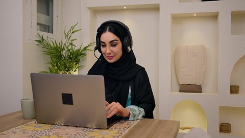 الاستمتاع بالمشروبات الساخنه ، عقد إجتماع عمل عبر الإنترنت،  جلسات هادئة في المنزل، مشاهدة الافلام والمسلسلات ، تصفح التطبيقات والمواقع، الاستماع الى الموسيقي عبر سماعات الاذن ،تصوير مقرب لامرأة عربية خليجية سعودية ترتدي العباءه والحجاب تجلس في المنزل، جلسة عمل عن بعد، سيدة اماراتيه تستخدم جهاز الحاسوب المحمول