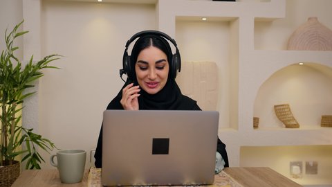 جلسات هادئة في المنزل، مشاهدة الافلام والمسلسلات ، تصفح التطبيقات والمواقع، الاستمتاع بالمشروبات الساخنه ، عقد إجتماع عمل عبر الإنترنت، الاستماع الى الموسيقي عبر سماعات الاذن ،تصوير مقرب لامرأة عربية خليجية سعودية ترتدي العباءه والحجاب تجلس في المنزل، جلسة عمل عن بعد، سيدة اماراتيه تستخدم جهاز الحاسوب المحمول