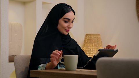 الاستماع الى الموسيقي عبر سماعات الاذن ،امرأة عربية خليجية سعودية ترتدي العباءه والحجاب تجلس في المنزل، إستخدام جهاز التابلت ، تصفح التطبيقات والمواقع، جلسة عمل عن بعد، عقد إجتماع عمل عبر الإنترنت، جلسات هادئة في المنزل، سيدة اماراتيه تشاهد الأفلام والمسلسلات ، الاستمتاع بالمشروبات الساخنه