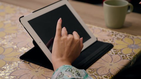 تصفح التطبيقات والمواقع، الاستمتاع بالمشروبات الساخنه ، عقد إجتماع عمل عبر الإنترنت، الاستماع الى الموسيقي عبر سماعات الاذن ،تصوير مقرب لامرأة عربية خليجية سعودية ترتدي العباءه والحجاب تجلس في المنزل، جلسة عمل عن بعد، جلسات هادئة في المنزل، سيدة اماراتيه تستخدم جهاز التابلت