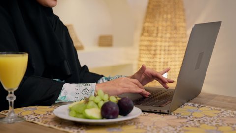 Fresh fruit slices and orange juice, enjoying a cold drink, integrating modern technology with daily routine, healthy lifestyle, close-up of a Saudi Arabian Gulf woman wearing abaya and hijab, sitting at a table at home using a mobile phone, Emirati lady enjoying a healthy breakfast, calm morning atmosphere