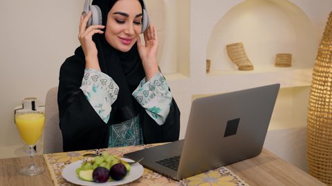 أجواء صباحية هادئة، الاستمتاع بشرب المشروبات الباردة ، شرائح الفاكهة الطازجة وعصير البرتقال، دمج التكنولوجيا الحديثة مع الروتين اليومي ، نمط حياة صحي، تصوير مقرب لامراه عربية خليجية سعودية ترتدي العباءة والحجاب، تجلس على طاولة في المنزل ويستخدم الهاتف المحمول ،سيدة اماراتية تستمتع بتناول وجبة فطور صحية