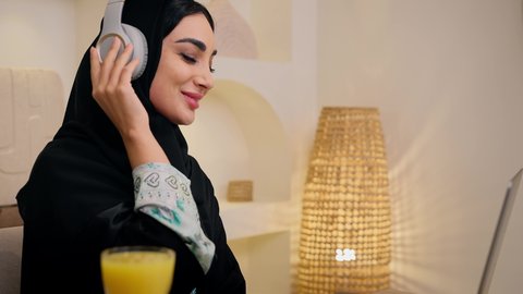 شرب عصير البرتقال، أجواء صباحية هادئة، الاستمتاع بشرب المشروبات الباردة ، دمج التكنولوجيا الحديثة مع الروتين اليومي ، نمط حياة صحي، تصوير مقرب لامراه عربية خليجية سعودية ترتدي العباءة والحجاب، تجلس على طاولة في المنزل ويستخدم الهاتف المحمول ،سيدة اماراتية تستمتع بتناول وجبة فطور صحية