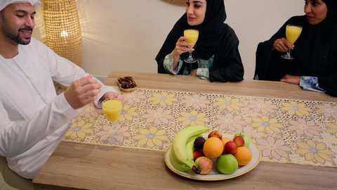 Friendly moments filled with love and harmony, gestures of pleasure and happiness, spending quality time, enjoying a cold drink, a warm family atmosphere, exchanging conversations among family members, a traditional hospitality session, an Emirati Arabian Gulf family sitting together around a table, exchanging fresh fruit.