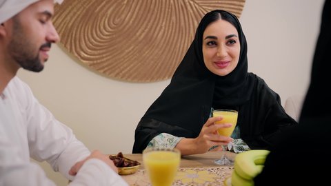 Gestures of joy and happiness, spending quality time, enjoying a cold drink, a warm family atmosphere, exchanging conversations among family members, a traditional hospitality session, an Emirati Arabian Gulf family sitting together around a table, exchanging fresh fruit, friendly moments filled with love and harmony.