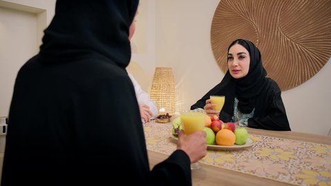 Spending a pleasant time, enjoying a cold drink, a warm family atmosphere, exchanging conversations among family members, a traditional hospitality session, an Emirati Arabian Gulf family sitting together around a table, exchanging fresh fruit, drinking orange juice, friendly moments filled with love and harmony.