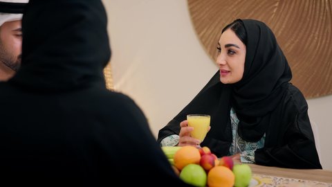 Enjoying a cold drink, a warm family atmosphere, exchanging conversations among family members, a traditional hospitality session, an Emirati Arabian Gulf family sitting together around a table, exchanging fresh fruit, drinking orange juice, friendly moments filled with love and harmony.