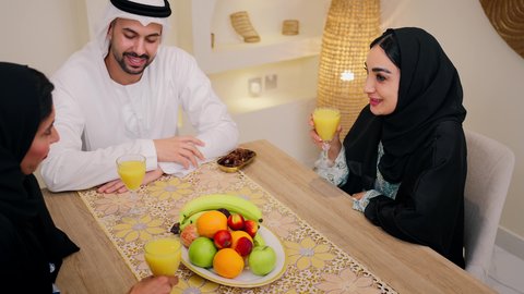 Family members chatting, a traditional hospitality session, an Emirati Gulf Arab family sitting together around a table, exchanging fresh fruit, drinking orange juice, friendly moments filled with love and harmony, a warm family atmosphere, enjoying a cold drink.